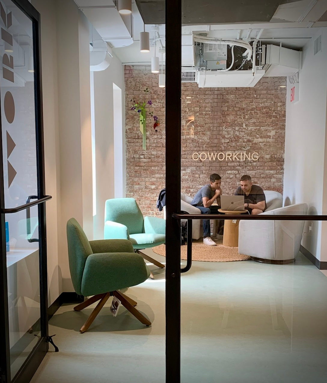 View of our coworking space entrance with two dads working together on a laptop sitting on our comfortable chairs..
