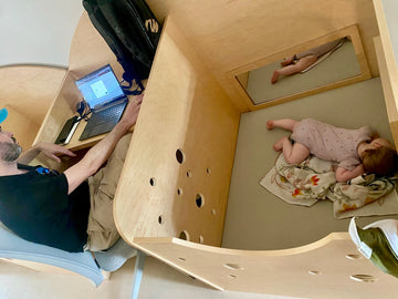 Photo of father at laptop and baby napping in TMC parent workstation